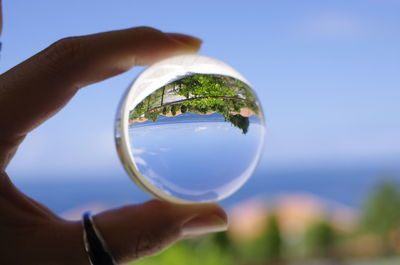 Close-up of cropped hand holding crystal ball against sky