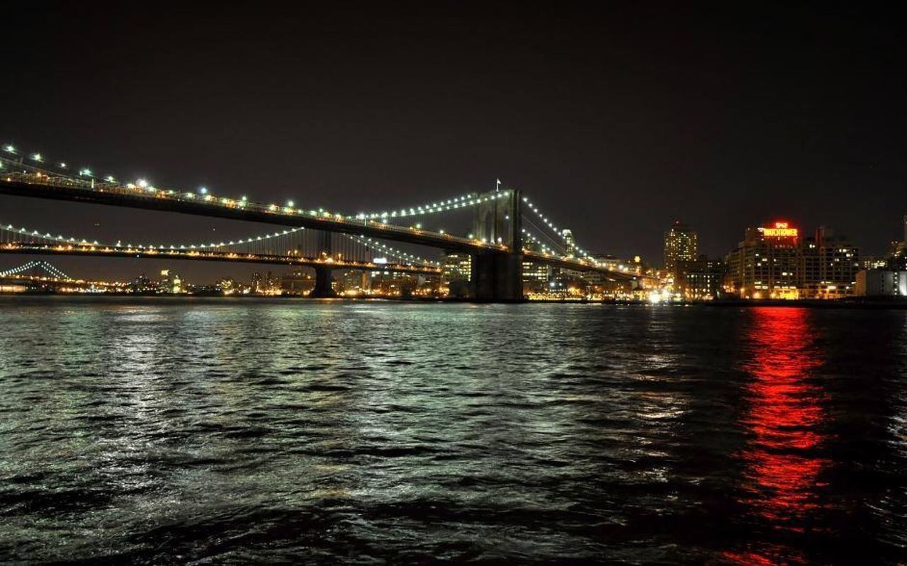 ILLUMINATED BRIDGE OVER RIVER WITH CITY IN BACKGROUND