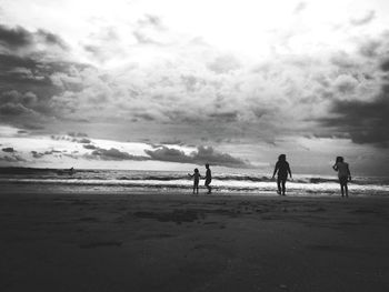 Silhouette people on beach against cloudy sky