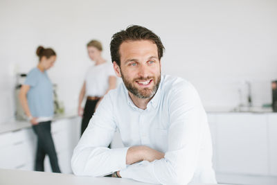 Mid adult man in office, people on background