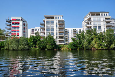 Buildings by lake against clear blue sky