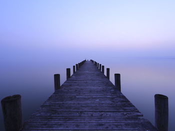 Pier over calm lake against sky during sunset