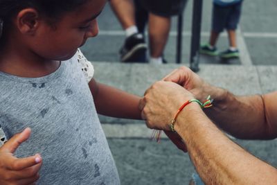 Cropped hands of man tying string on girl arm