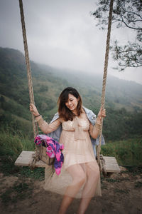 Full length of smiling woman standing on swing against plants