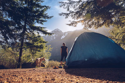 Rear view of woman with dog standing on field at campsite against sky