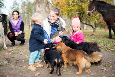 Happy family-mother with  children hugging and feeds pets dogs, cats and goats in countryside farm