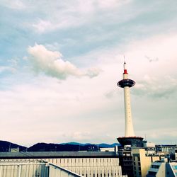 Communications tower by river against cloudy sky