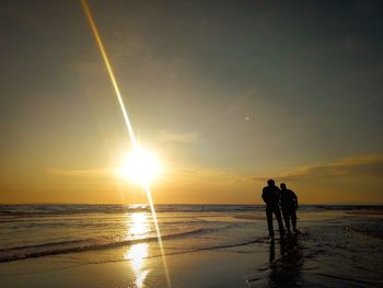 Silhouette people on beach against sky during sunset