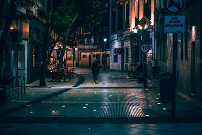 Illuminated street light on road by building at night