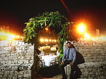 Man standing against illuminated wall at night