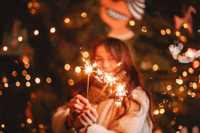 Teenage girl holding sparklers standing by luminous christmas tree