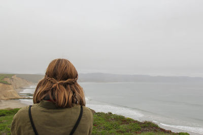 Woman overlooking calm sea against clear sky