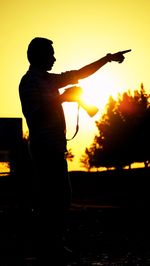 Silhouette man holding orange sun against sky during sunset