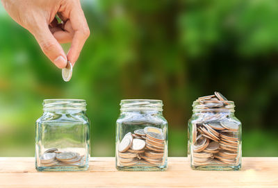 Cropped hand putting coins in jar on wooden table