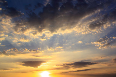 Low angle view of sunlight streaming through clouds during sunset