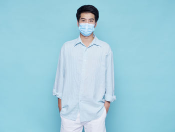 Portrait of young man wearing mask standing against blue background