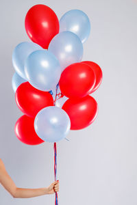 Cropped hand of woman with balloons against white background