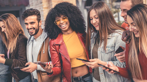 Smiling friends using smart phone while standing outdoors