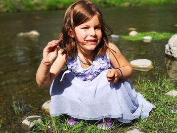 Portrait of cute girl crouching on grassy land by lake