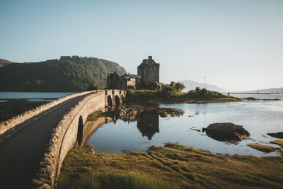 Bridge leading towards castle in sea against clear sky