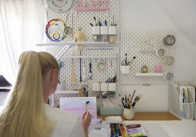 Back view of a blonde girl draws in a home studio equipped in modern design.