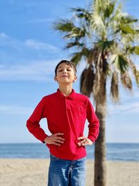 Portrait of young man standing at beach against sky