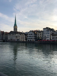 View of buildings by river against cloudy sky