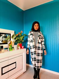 Portrait of young woman standing against wall at home