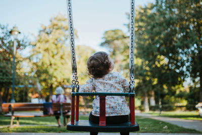 Rear view of baby girl sitting on swing at park