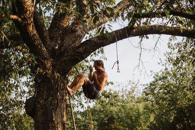 Shirtless man climbing on tree