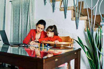 Young executive woman working from home while taking care of her young daughter