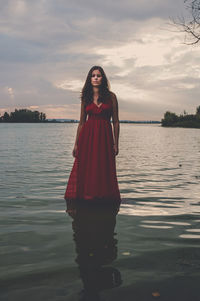 Portrait of woman standing in lake against sky during sunset