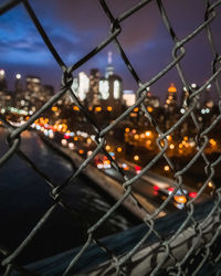 Close-up of chainlink fence against illuminated city at night