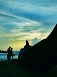 Silhouette man photographing at beach against sky during sunset