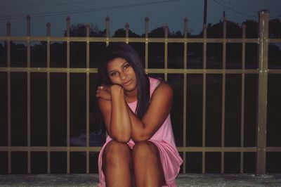 Young woman sitting on railing against sky