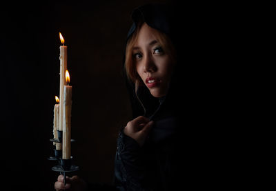 Close-up portrait of young woman by lit candles against black background