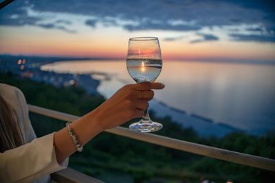 Reflection of hand holding glass of water against sky in sunset time