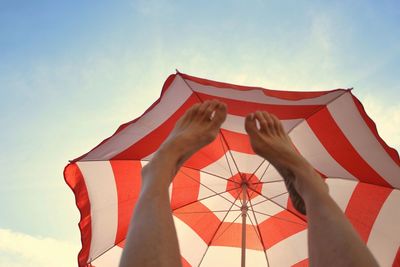 Low angle view of legs under beach umbrella against sky
