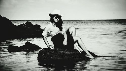 Woman sitting in sea against sky