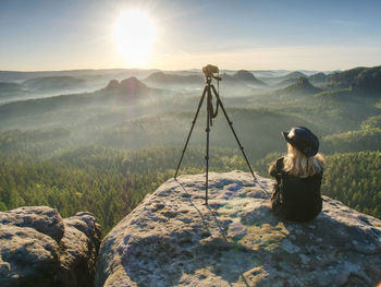 Rear view of woman sitting on rock. photographer artist work in morning mountains