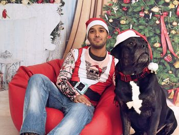 Portrait of man with dog sitting against christmas tree