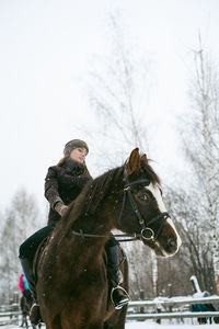 Low angle view of beautiful woman riding horse on snow covered field