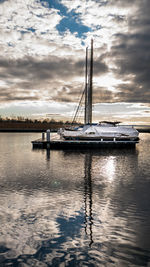 Sailboats moored in sea against sky during sunset