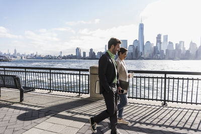 Usa, man and woman walking at new jersey waterfront with view to manhattan