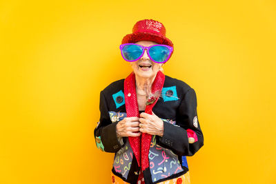 Portrait of smiling senior woman against yellow background