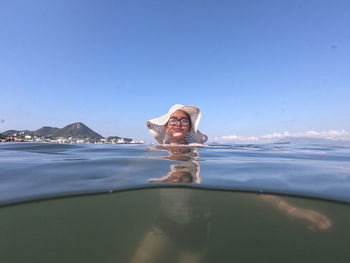 Portrait of teenage girl wearing hat while swimming in sea against blue sky