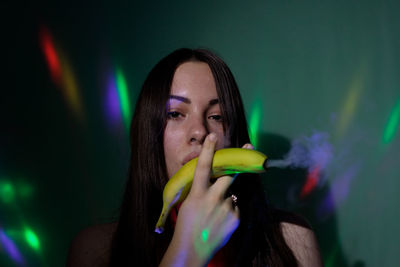 Close-up portrait of woman holding banana against wall