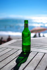 Green bottle on table at beach against sky