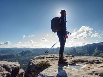 Tall tourist or hiker man with backpack and trekking poles hiking on rocky mountain peak