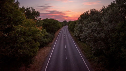 Empty road amidst trees against sky during sunset